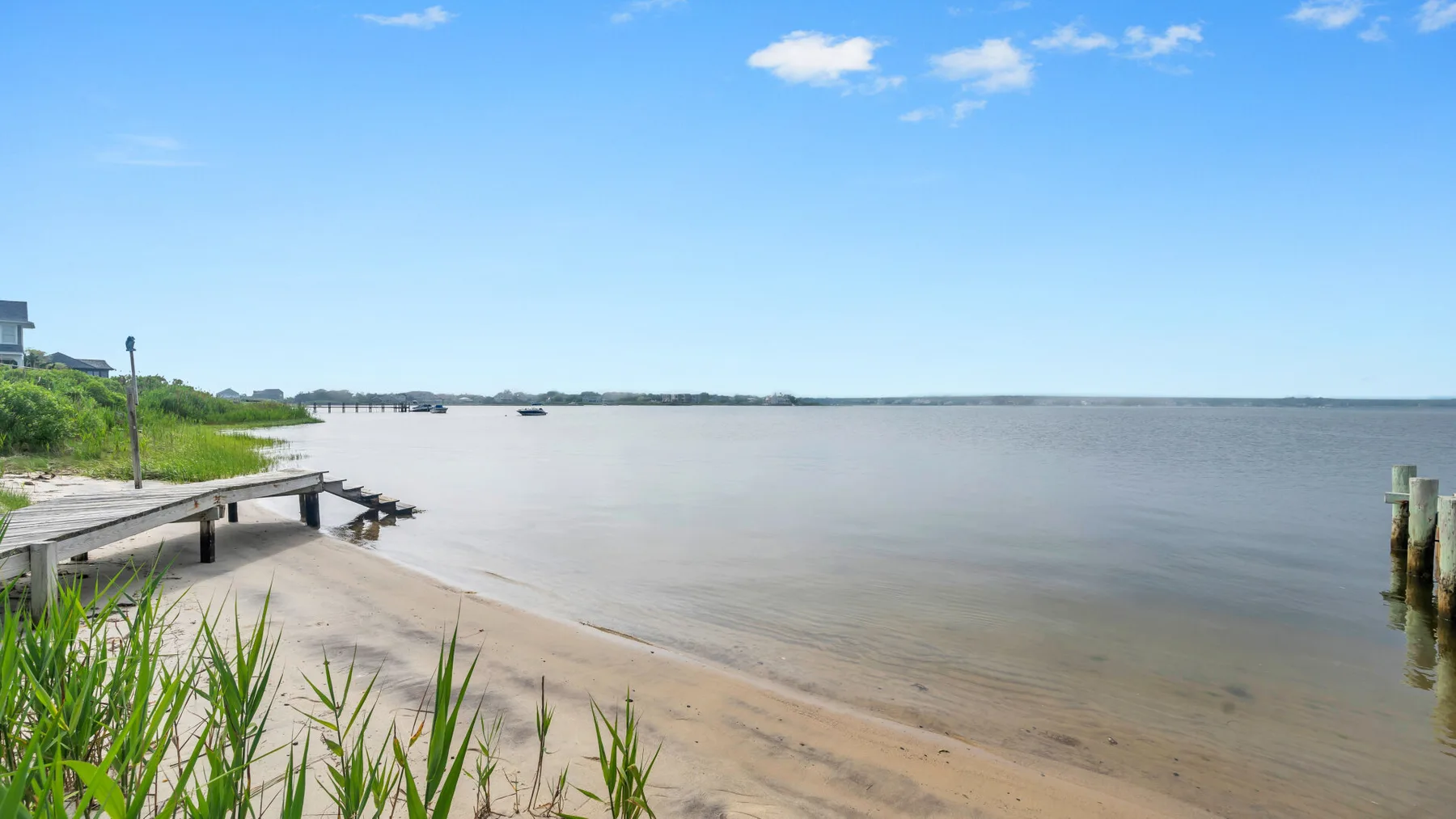 Una orilla arenosa se encuentra con aguas tranquilas junto a un muelle de madera.