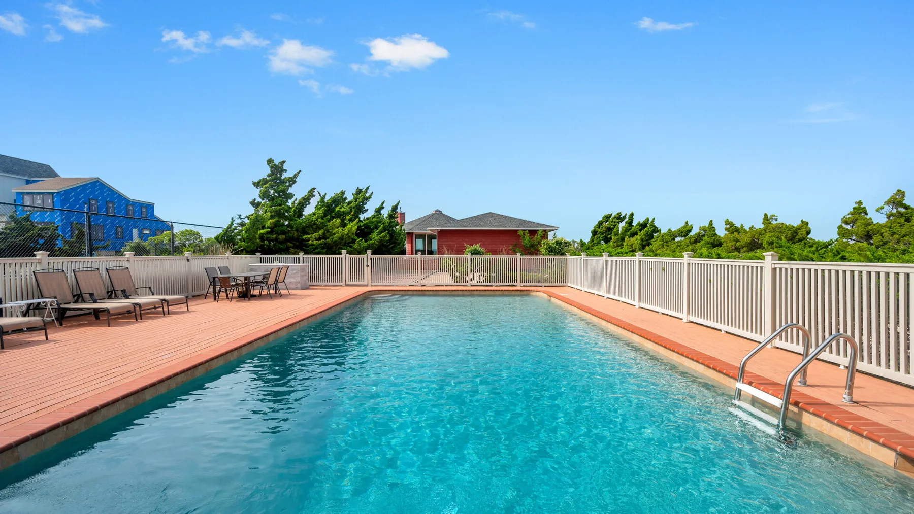 Una piscina al aire libre está rodeada por una terraza de madera y una barandilla blanca.