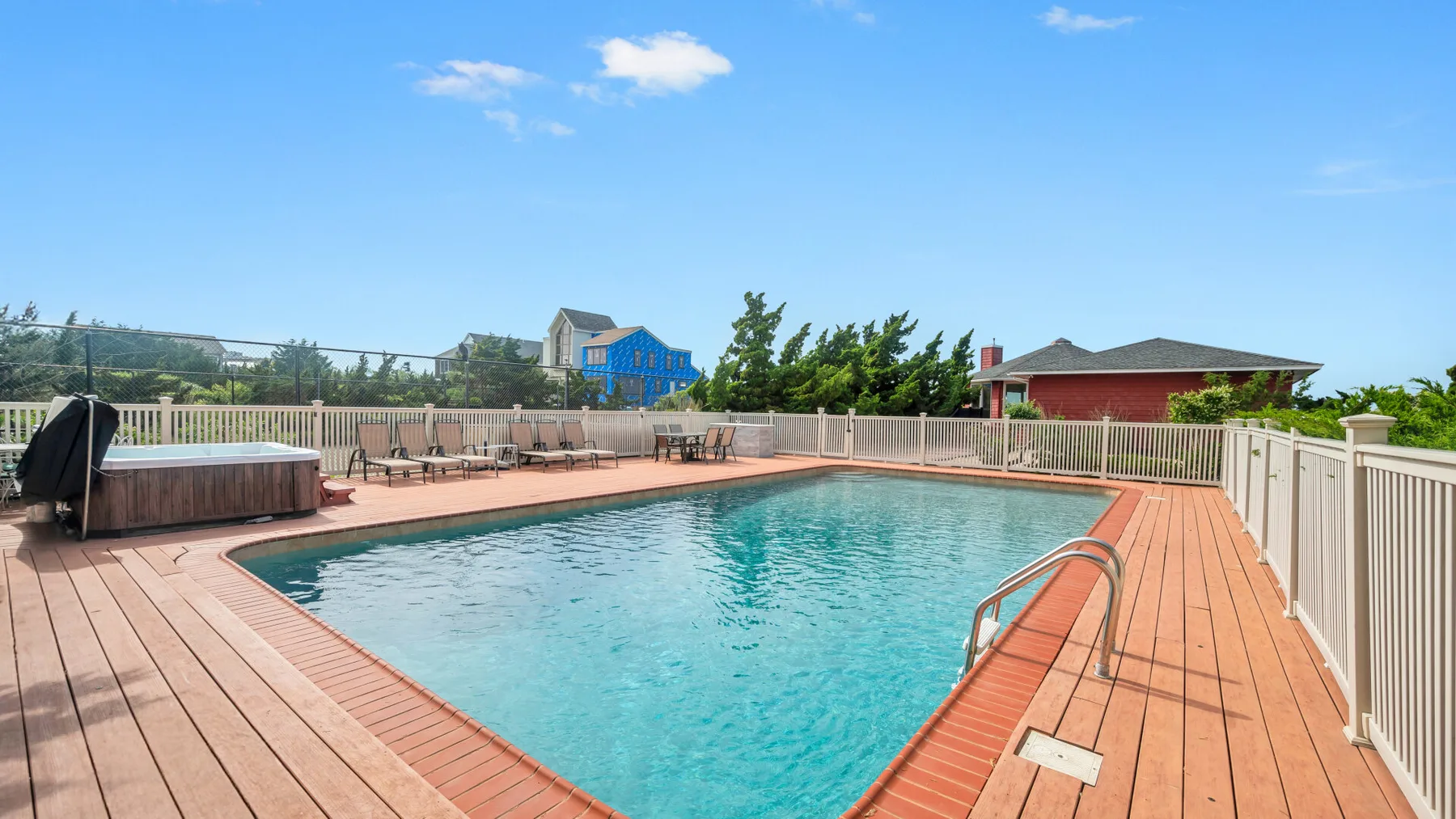 An outdoor swimming pool is surrounded by a wooden deck and white railing.