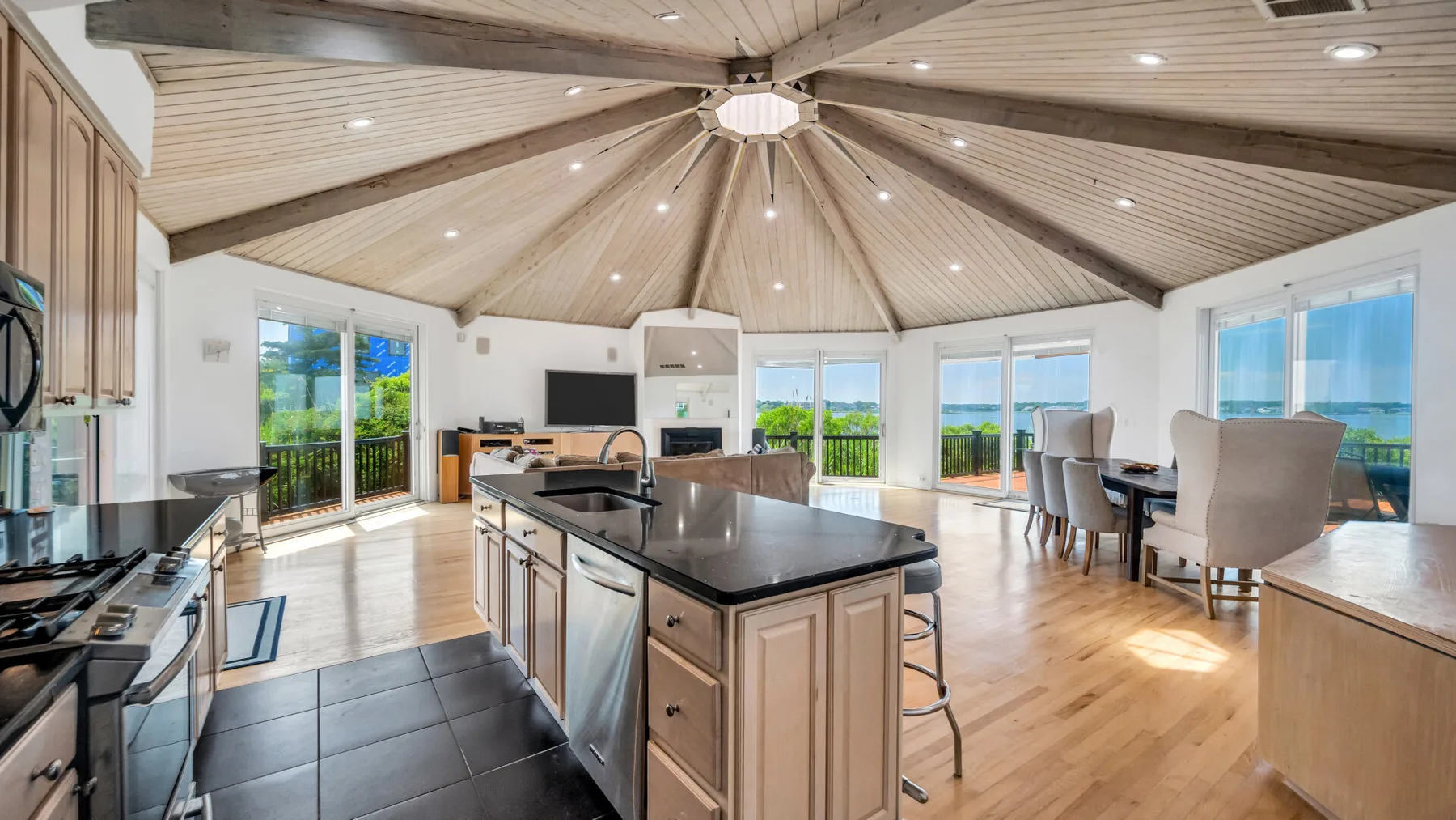 Una cocina y comedor diáfanos y luminosos, con techo alto de madera y grandes ventanas.
