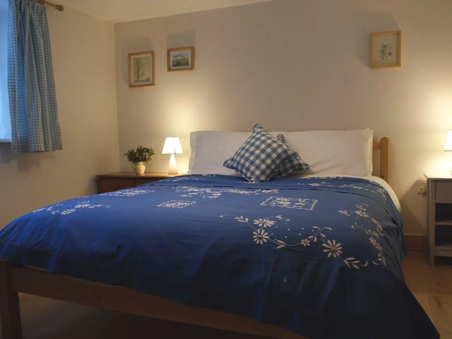 Un dormitorio con una cama con ropa de cama de flores azules y una almohada de cuadros en The Stone Barn Cottage, en Holne