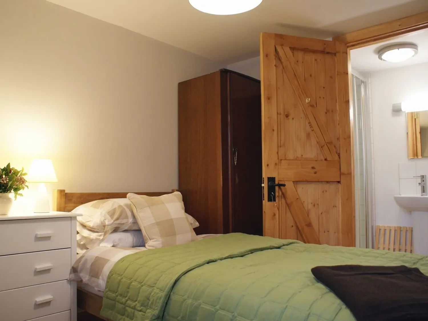 Un dormitorio con una cama cubierta por una colcha verde y una puerta de madera abierta al baño.