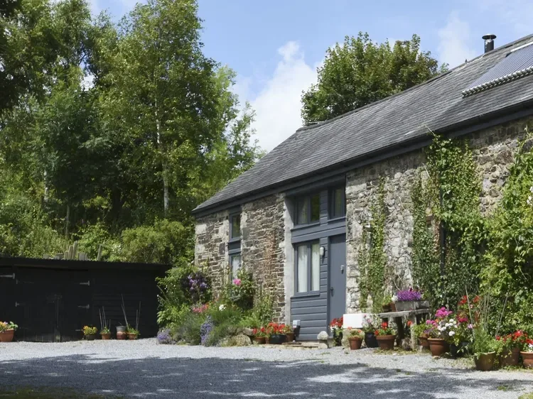 A stone cottage with a gray door and flowering plants along the front.