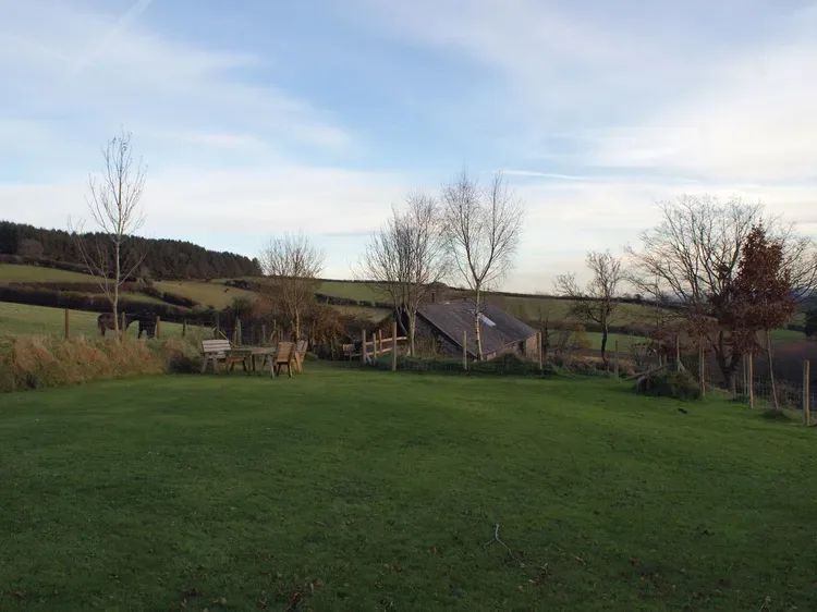 Un amplio jardín de césped con asientos al aire libre y un edificio pequeño al fondo.