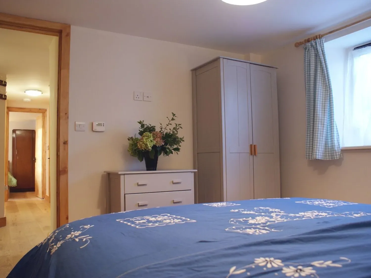 Un dormitorio con una colcha azul estampada y un armario junto a una ventana.