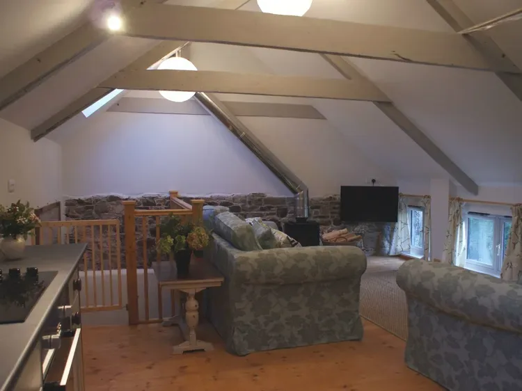 An attic living room with seating, exposed beams, and low windows.
