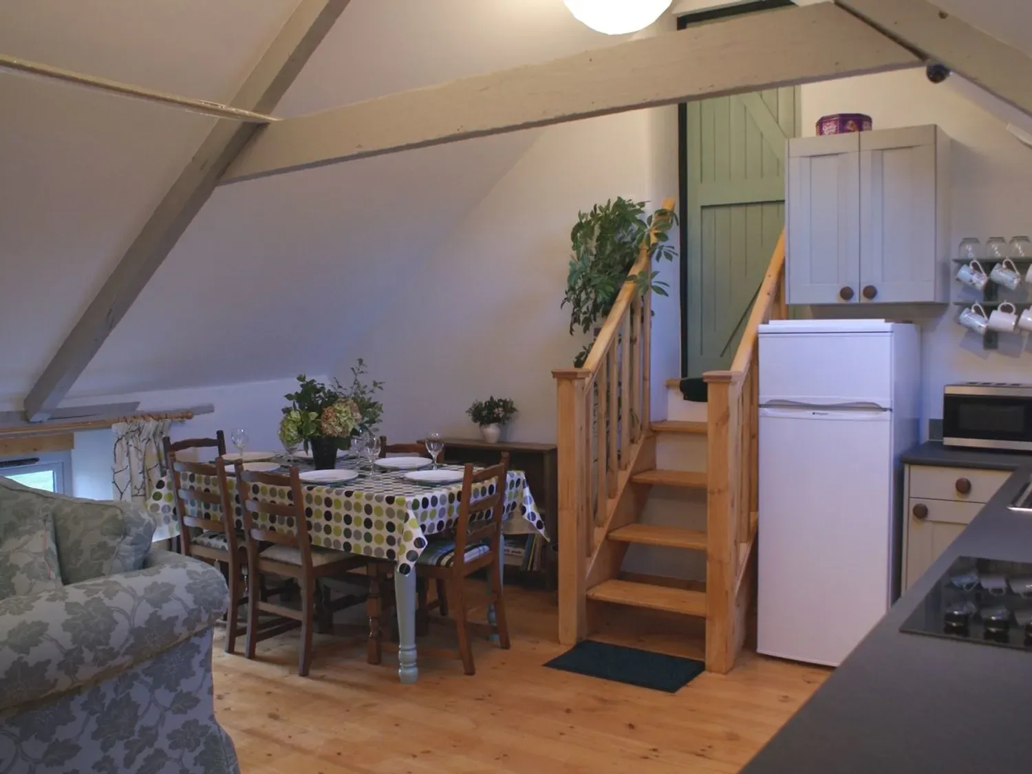 Una zona de comedor con la mesa puesta está junto a unas escaleras de madera y una cocina.