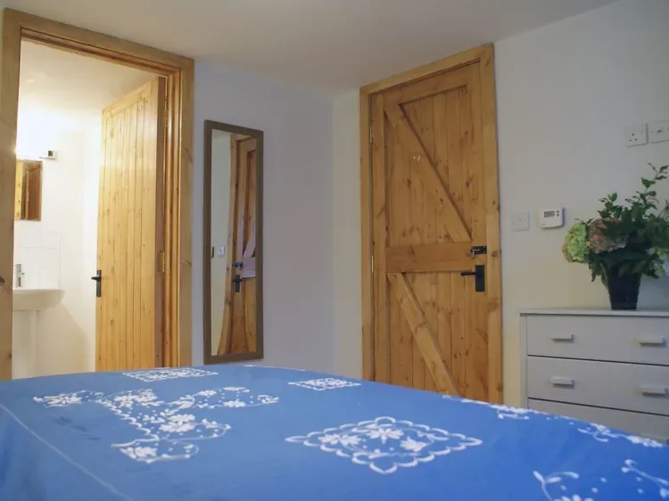 Un dormitorio con una colcha azul estampada, puertas de madera y una cómoda.