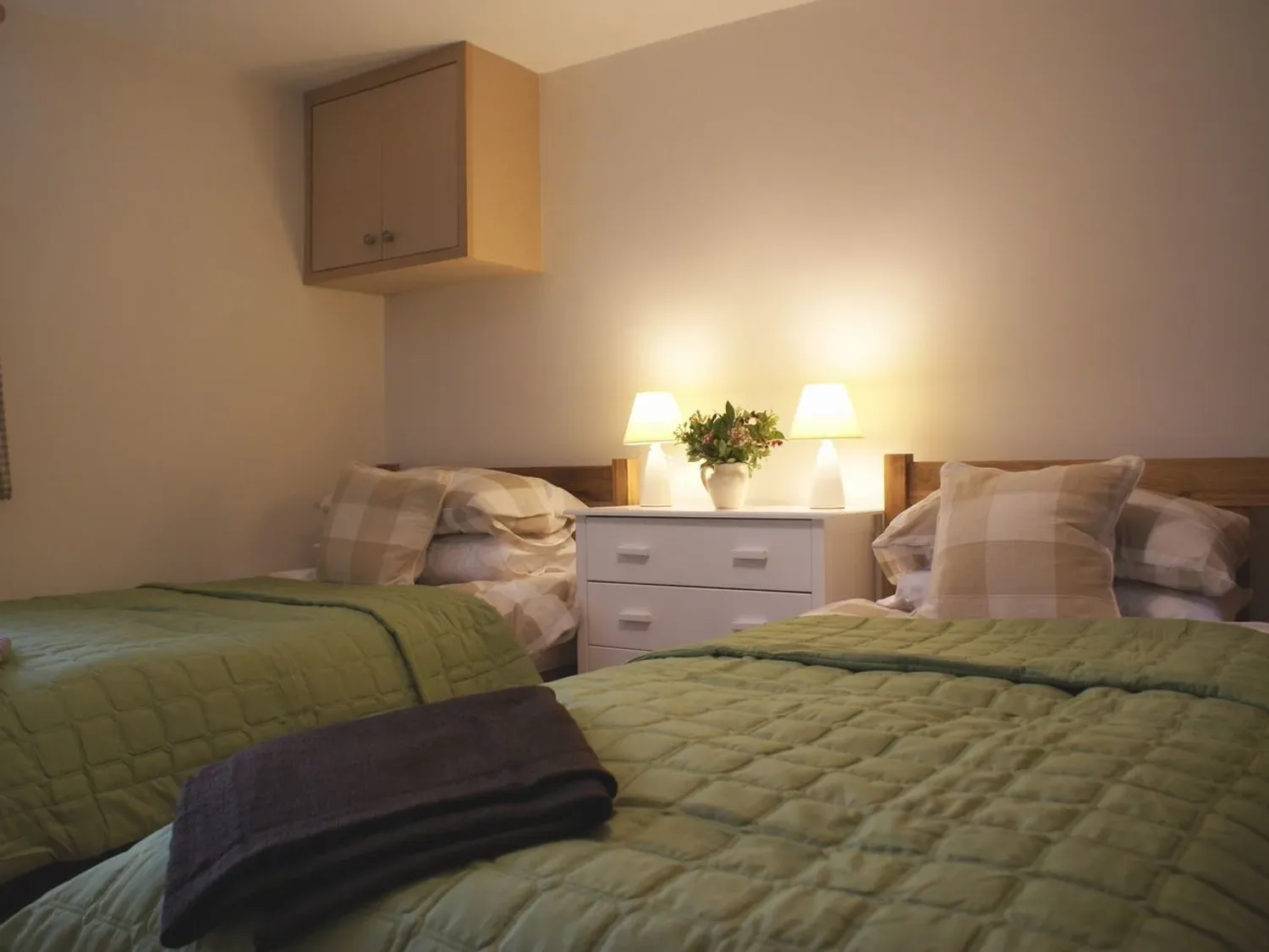 Un dormitorio con dos camas individuales, colchas verdes y una cómoda blanca con dos lámparas y un jarrón en The Stone Barn Cottage, en Holne
