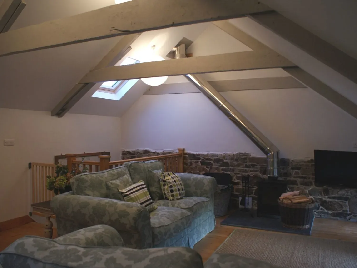 Un salón con un sofá, una estufa de leña y una claraboya en The Stone Barn Cottage, en Holne