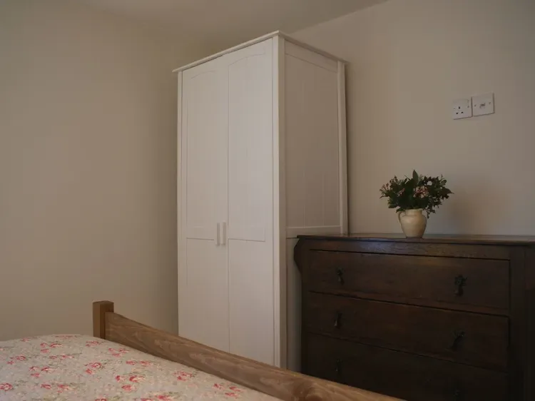 Un rincón de dormitorio con un armario blanco, una cómoda oscura y ropa de cama floral.