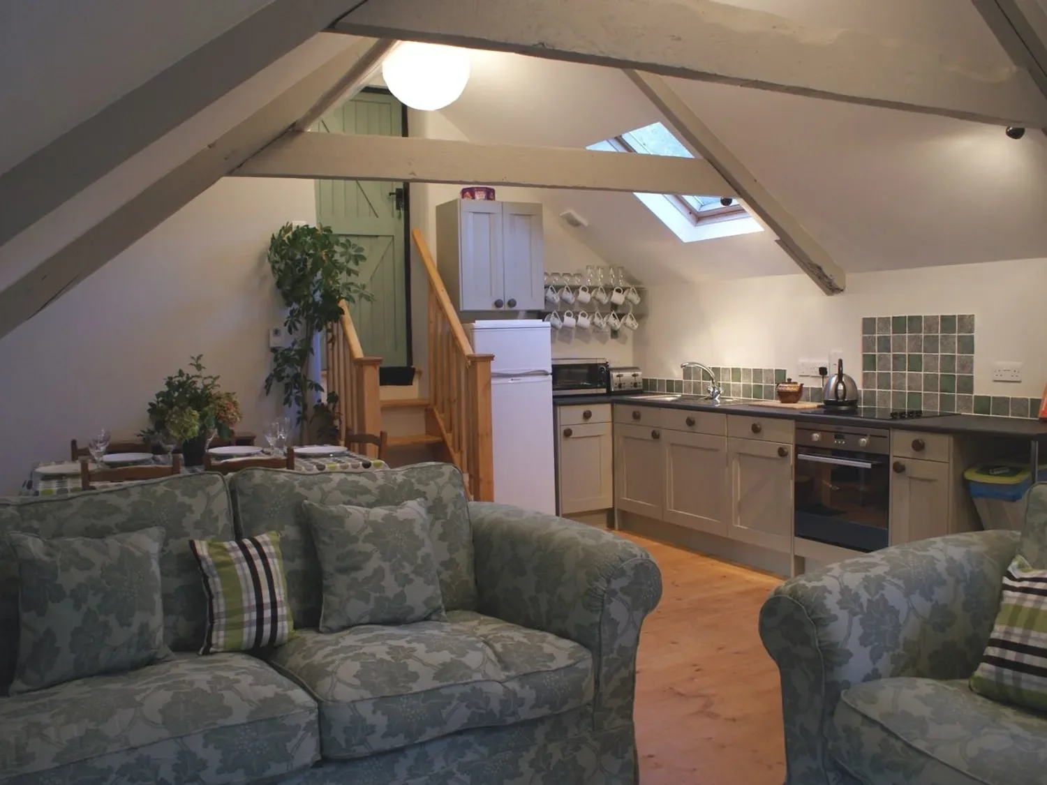 Una cocina y zona de estar con una escalera, un frigorífico y sofás estampados en The Stone Barn Cottage, en Holne