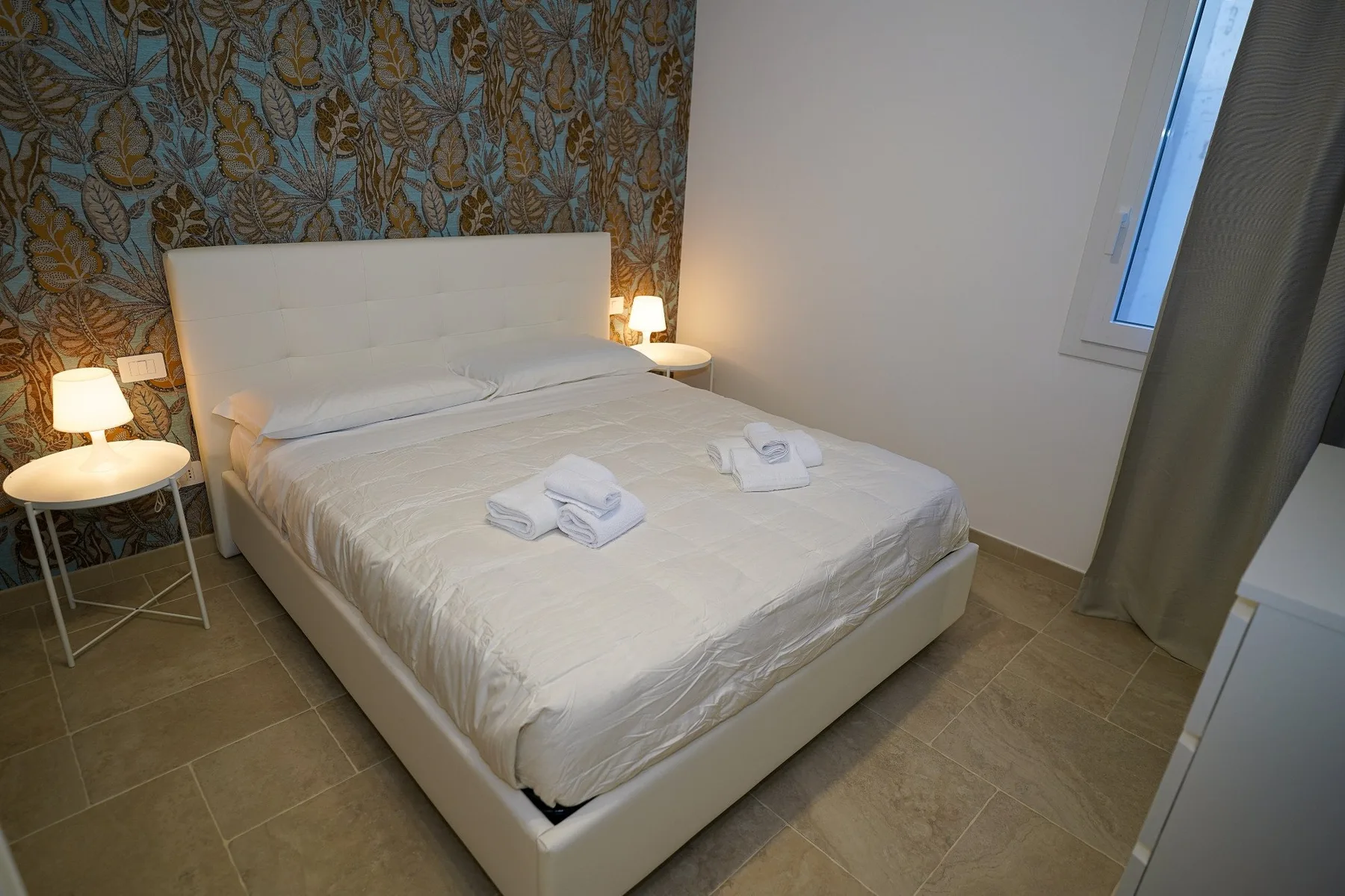Un dormitorio con una cama bien arreglada, mesitas de noche y papel pintado estampado.