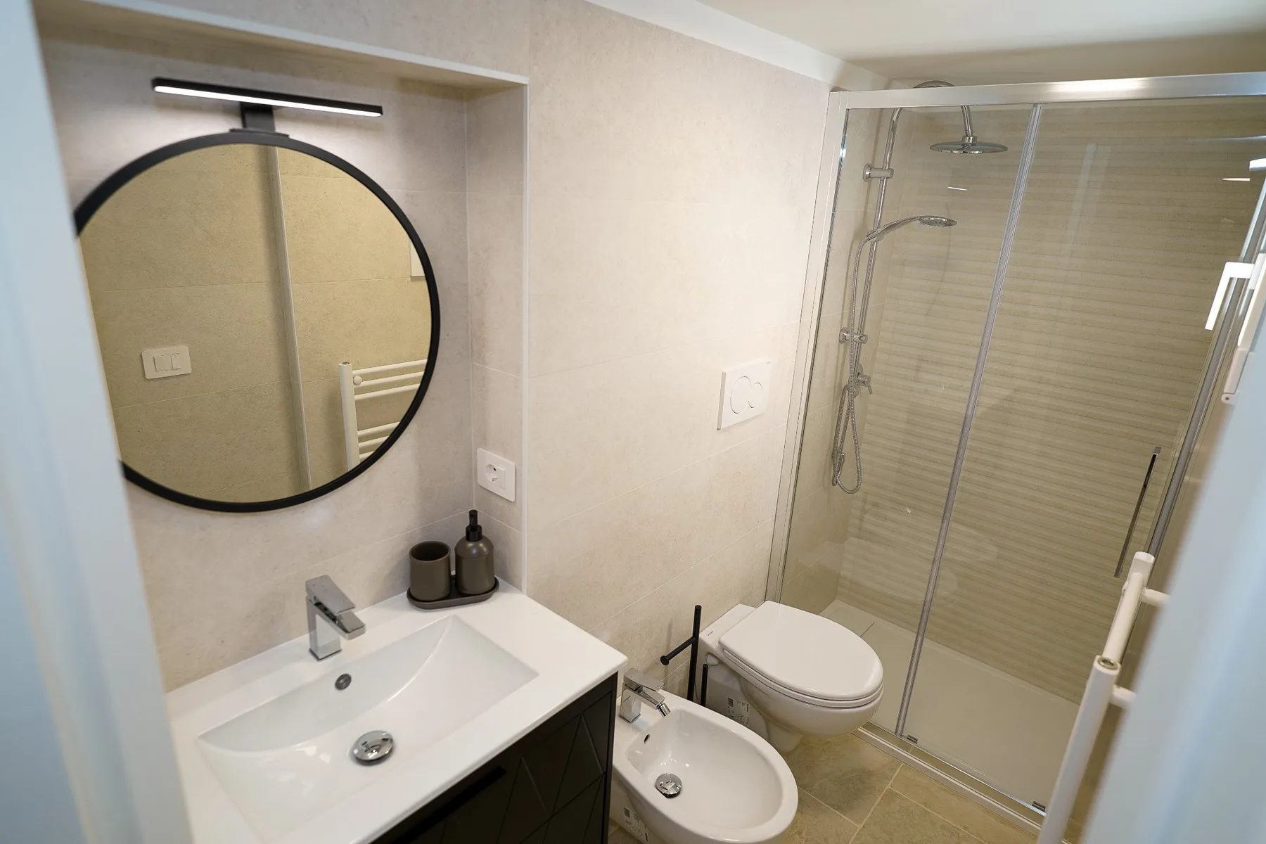 Un baño con lavabo, espejo redondo, inodoro, bidé y ducha.