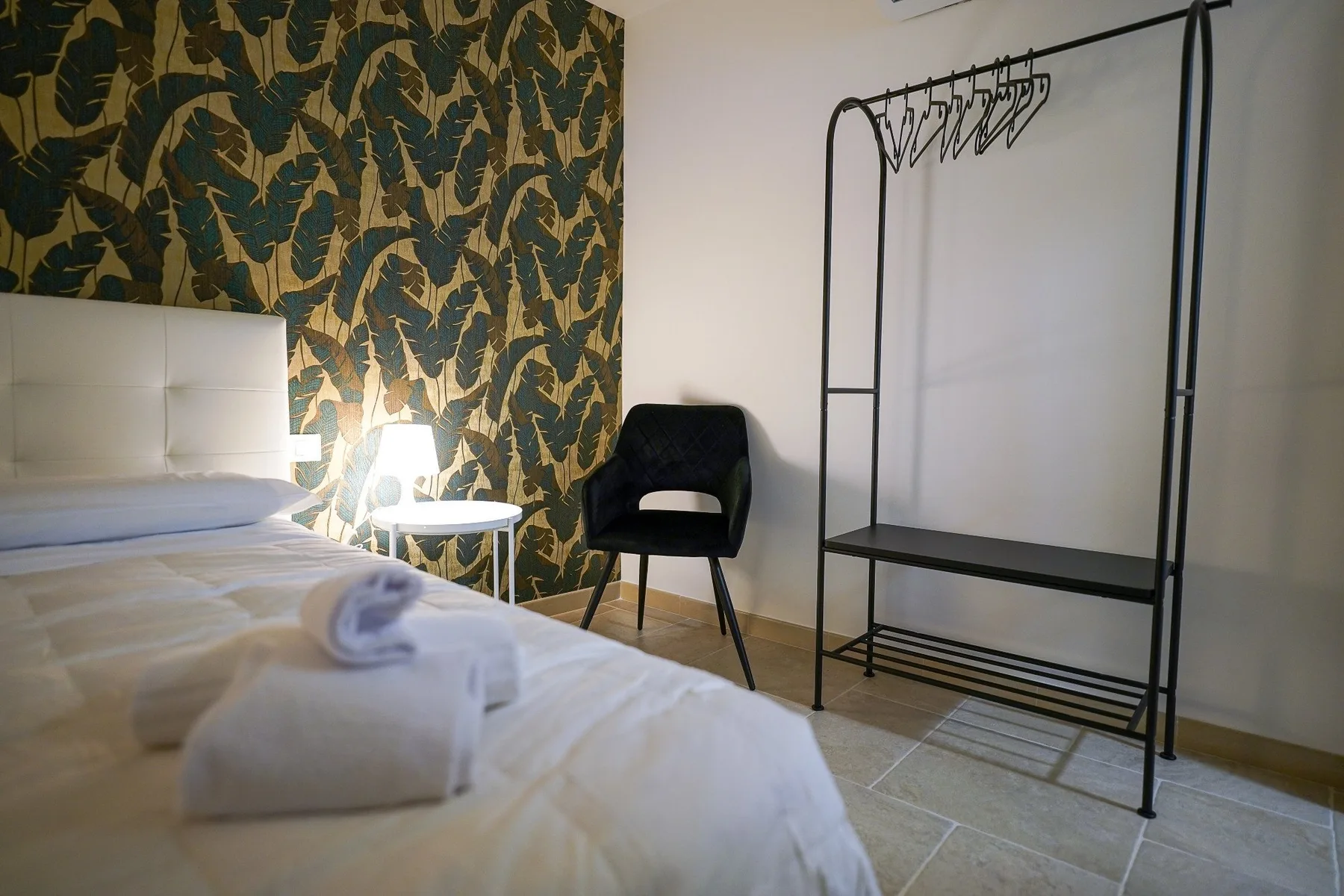Un dormitorio con una cama, una silla y un perchero abierto.