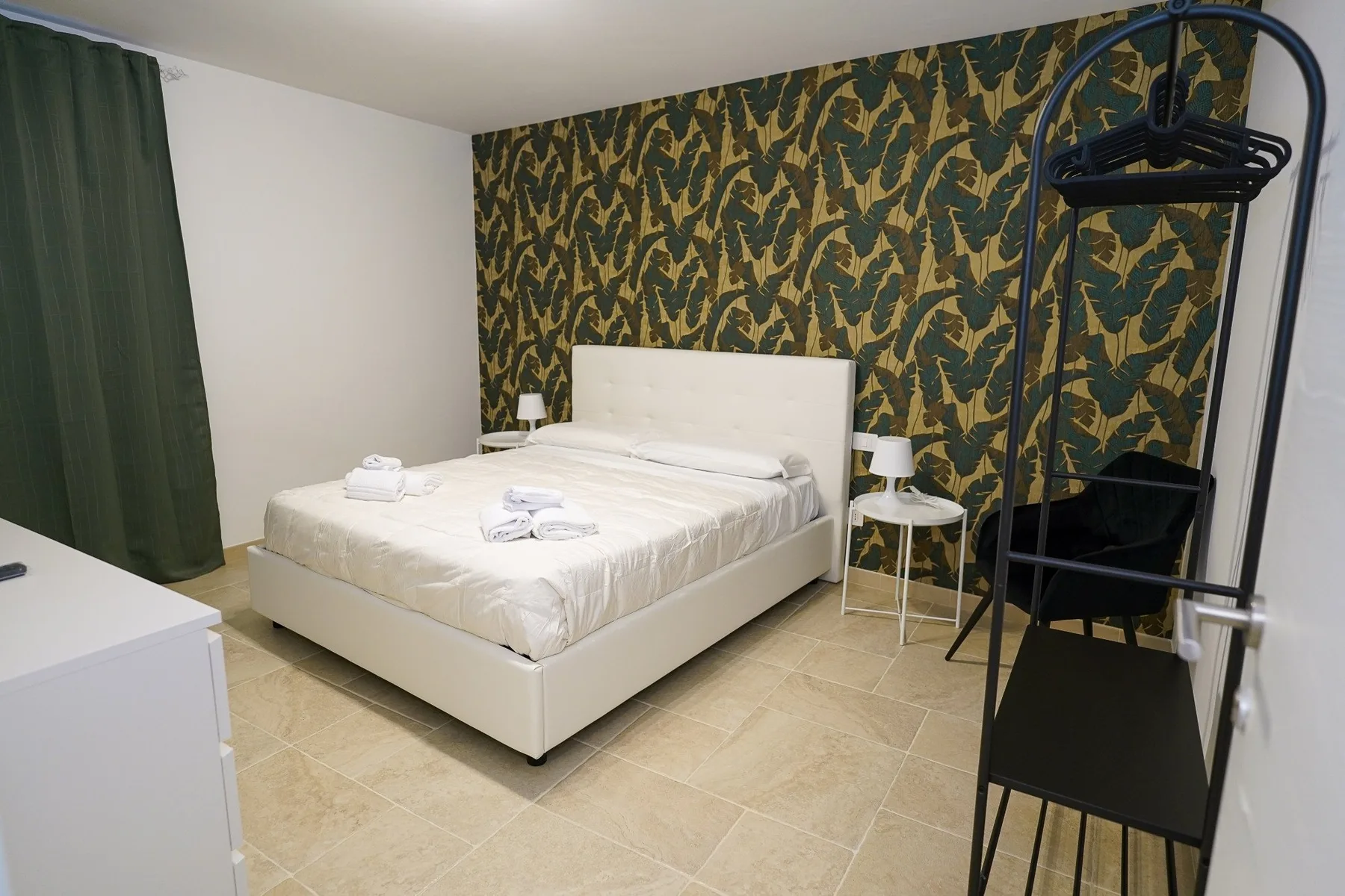 Un dormitorio con una cama doble, una pared estampada y cortinas verde oscuro.