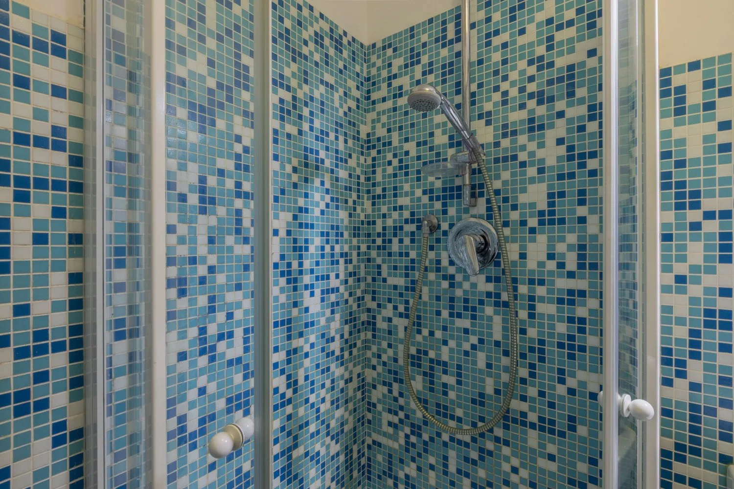 A tiled shower with blue mosaic walls and a handheld showerhead.