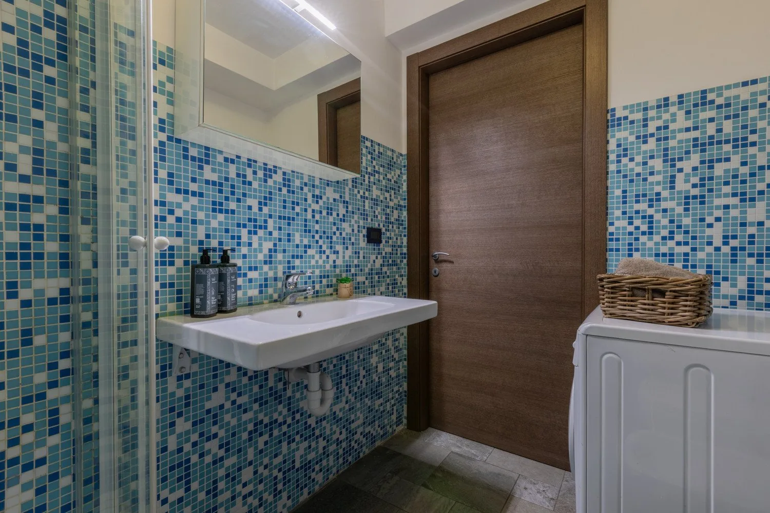 A tiled bathroom with a wall-mounted sink and a wooden door.