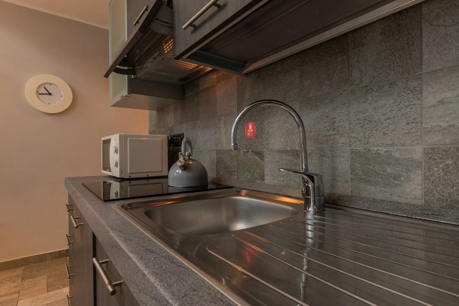 A kitchen counter with a stainless steel sink, microwave, and kettle.