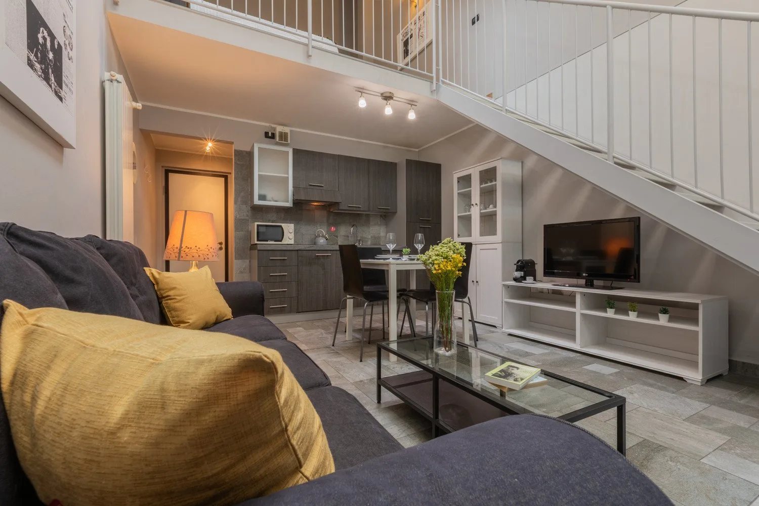 A living room with a sofa, glass coffee table, and television beneath a staircase.