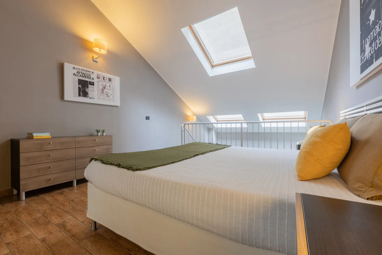 A bright bedroom with a bed beneath sloped ceilings and a skylight.