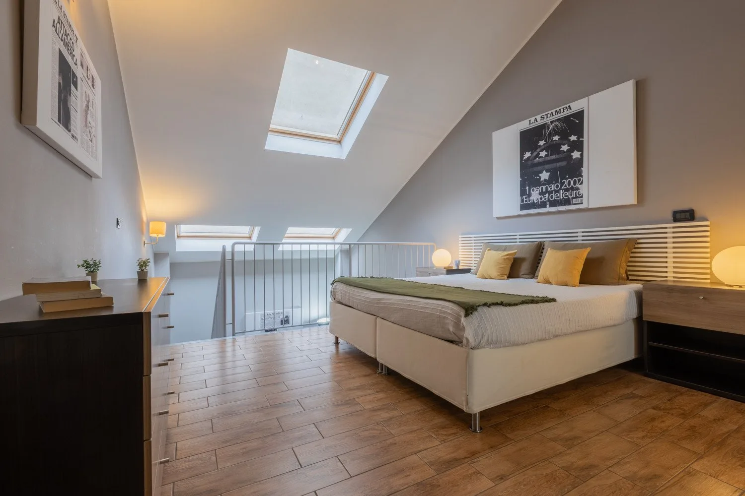 A bedroom with a large bed beneath skylights and a framed wall print.