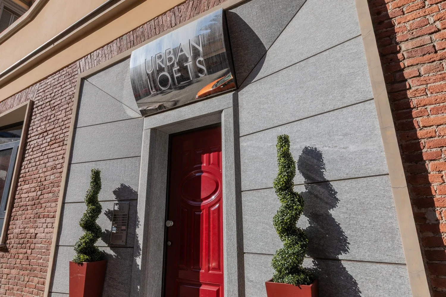 A red entrance door sits beneath a sign on a gray facade.
