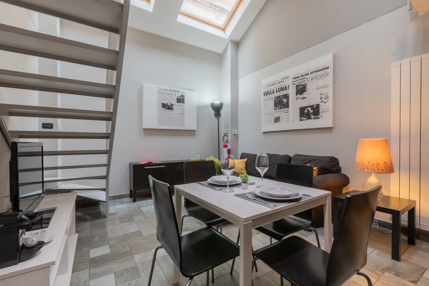 A dining area with a set table, dark seating, and framed wall prints.
