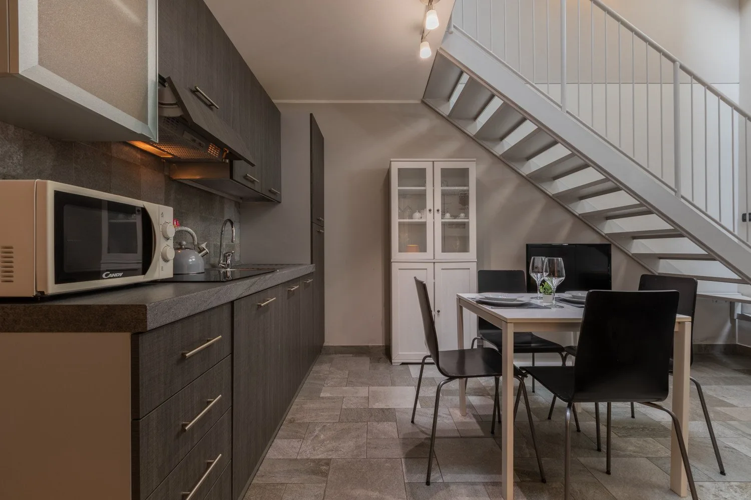 A kitchen and dining area beneath a staircase, with a table and dark cabinetry.