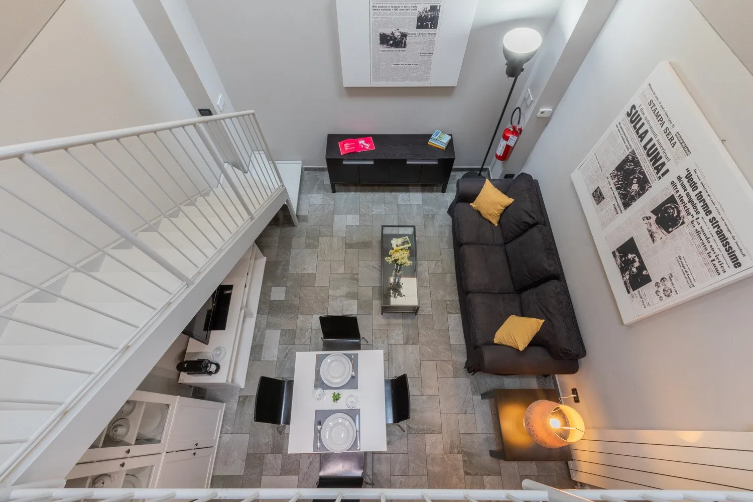 A double-height living room has a dark sofa, a coffee table, and a dining area.