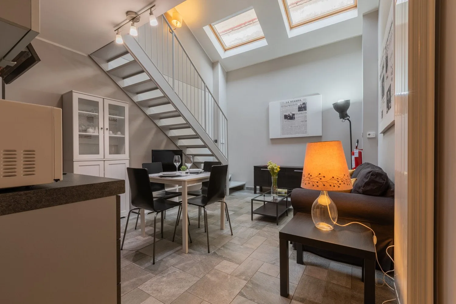 A bright open-plan living and dining area sits beneath a staircase and skylights.