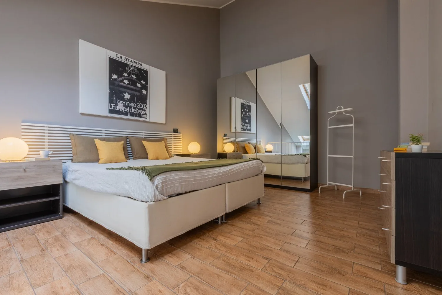 A bedroom with a low bed, mirrored wardrobe, and wood-look flooring.