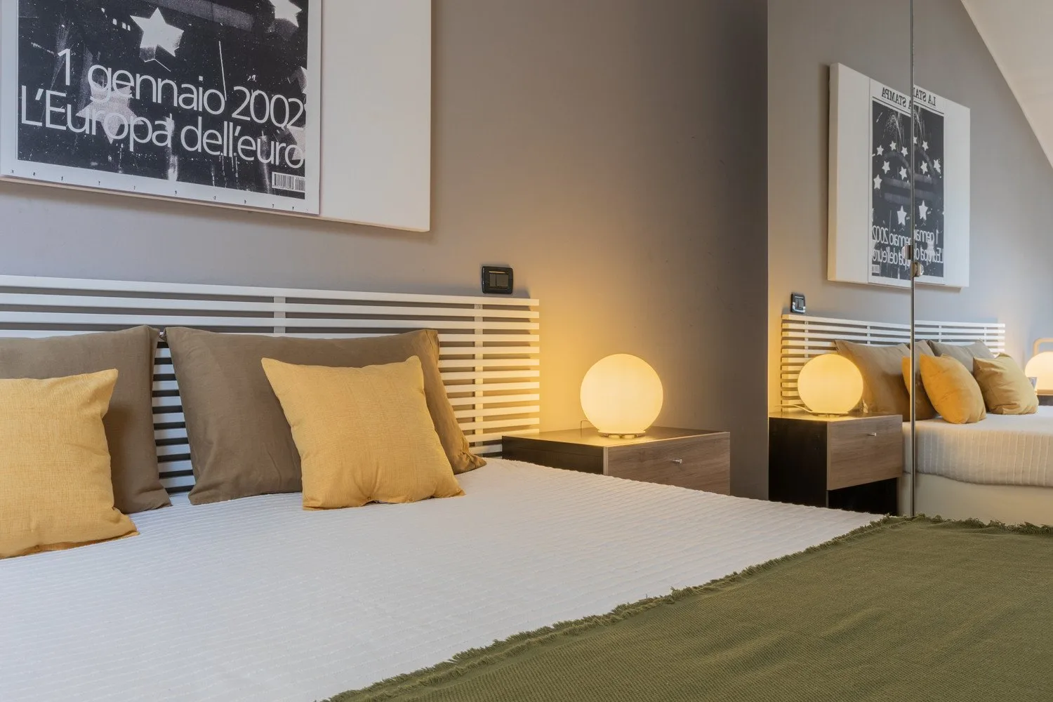 A bedroom with a neatly made bed, warm bedside lighting, and framed wall art.