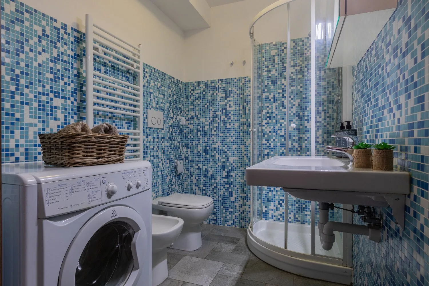A tiled bathroom with a washing machine, toilet, sink, and curved shower enclosure.