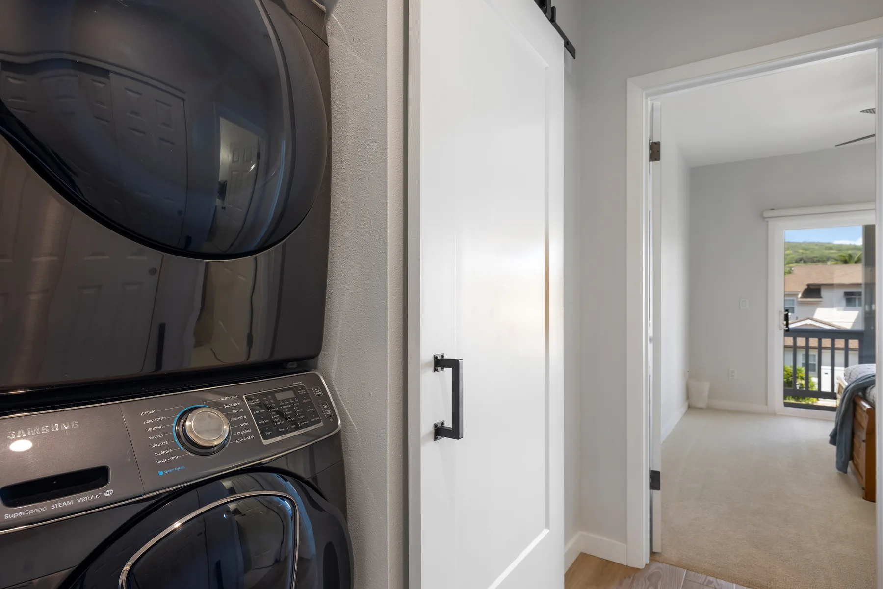 Zona de lavandería con lavadora y secadora apiladas junto a un dormitorio.