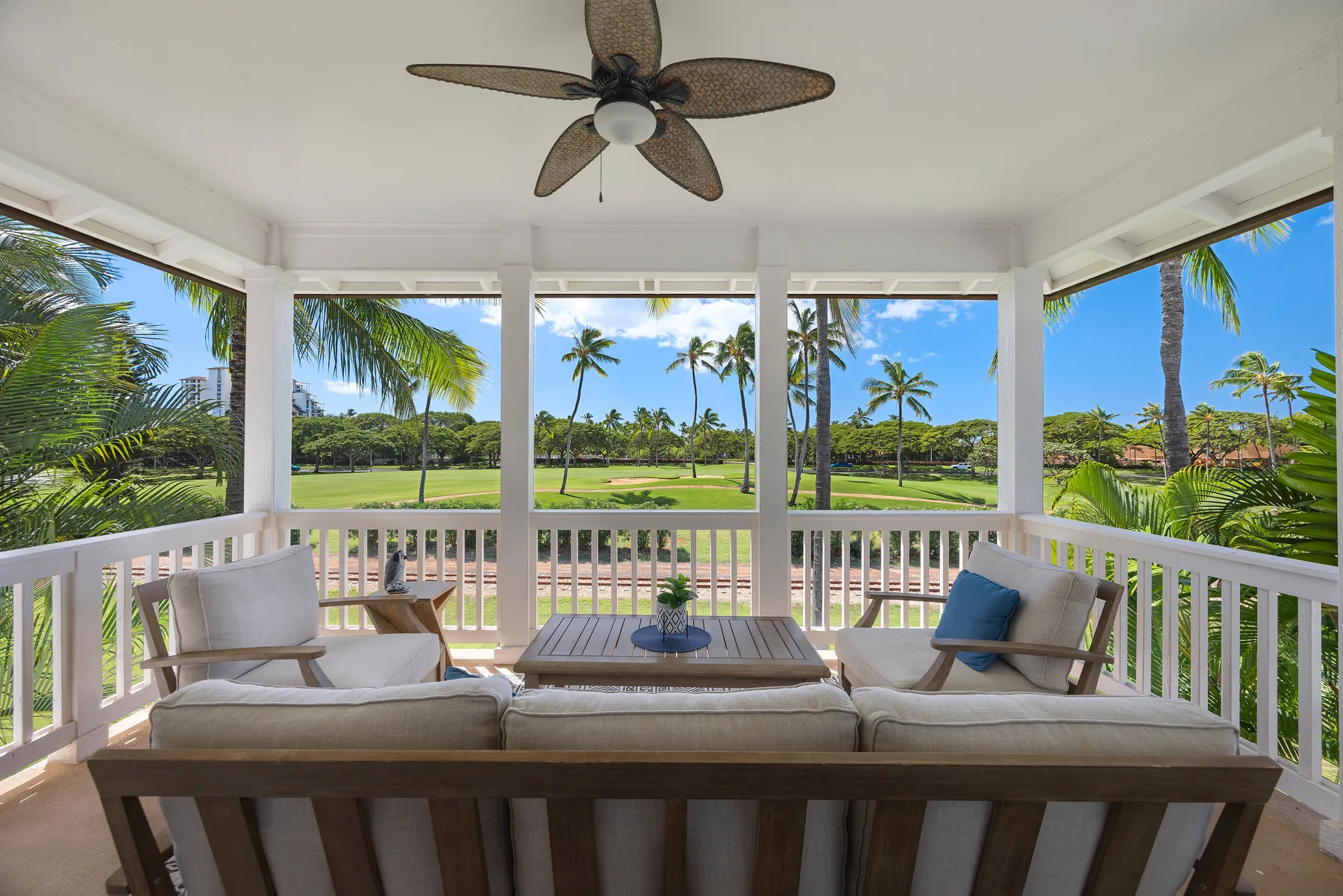 A covered outdoor seating area overlooks a green lawn and palm trees.