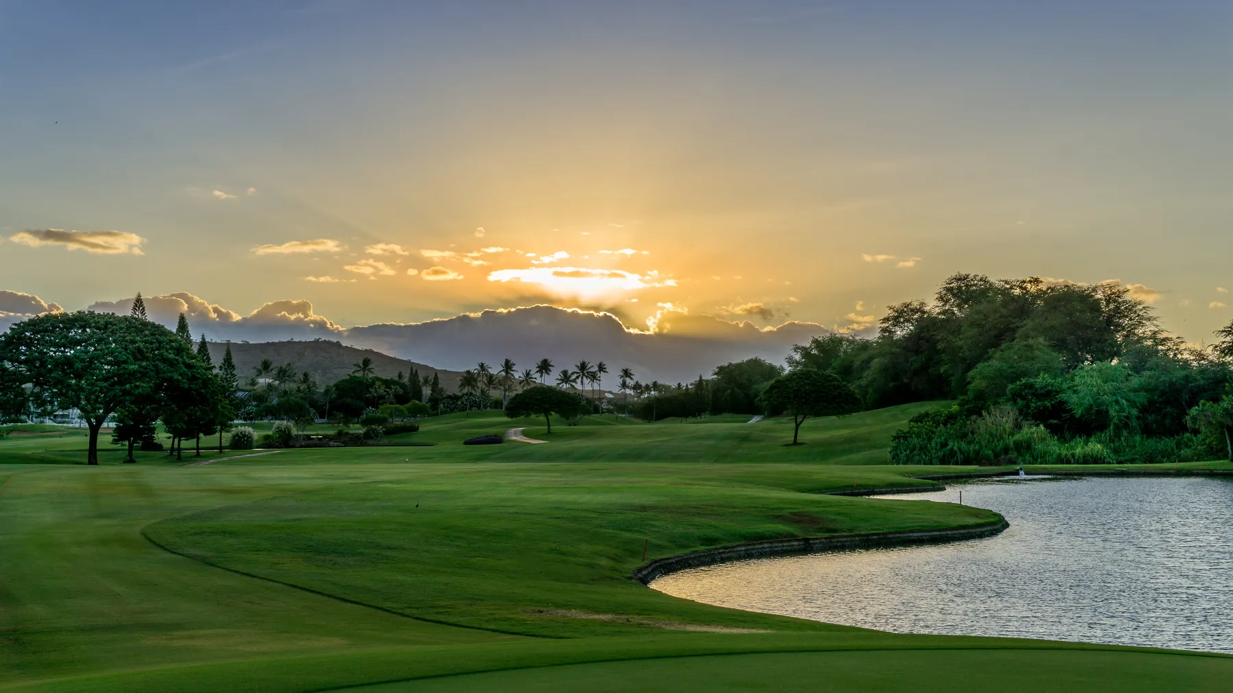 A golf course at sunset, with a pond beside the fairway.