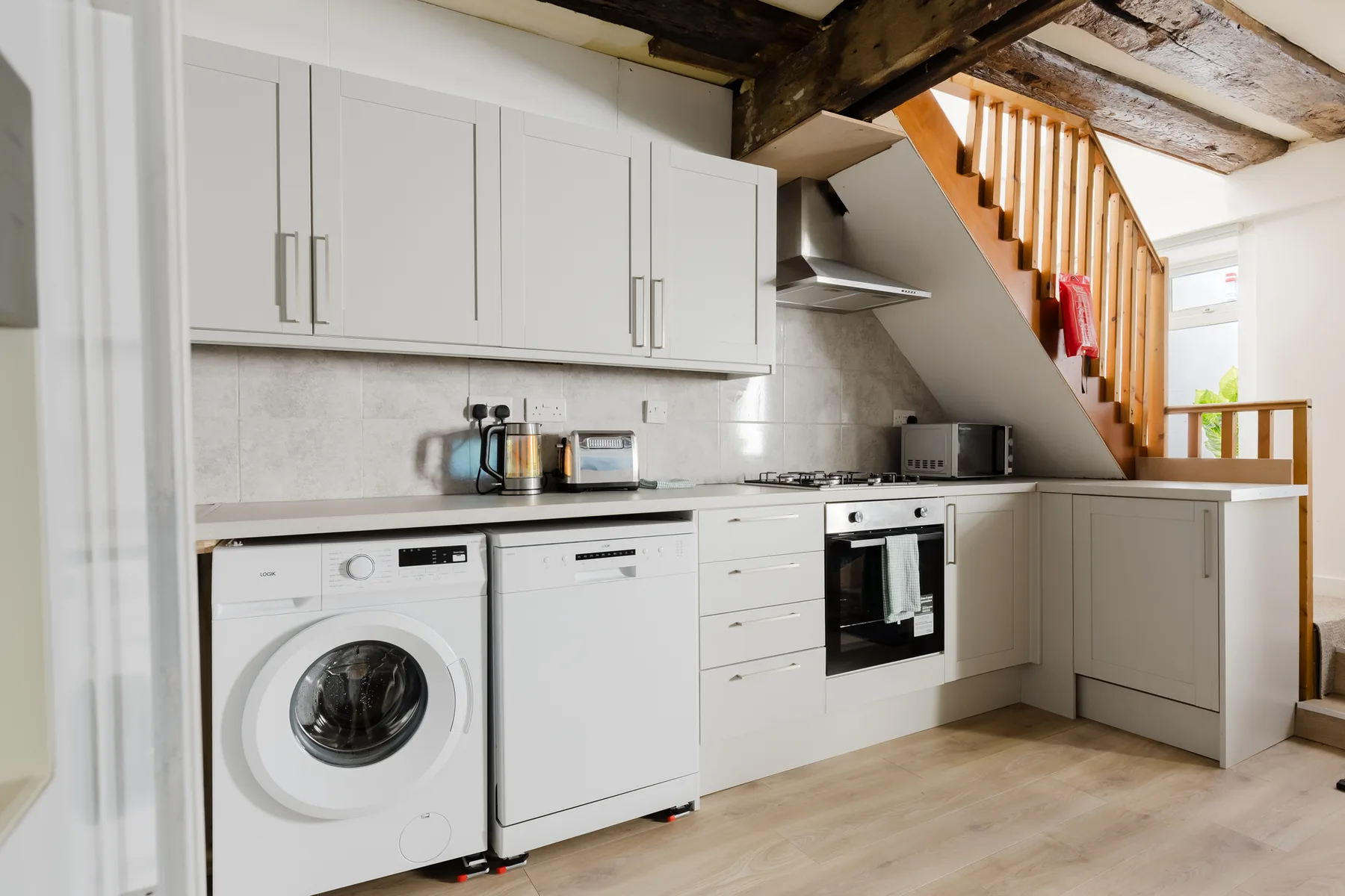 A kitchen with white cabinets, appliances, and a wooden staircase.
