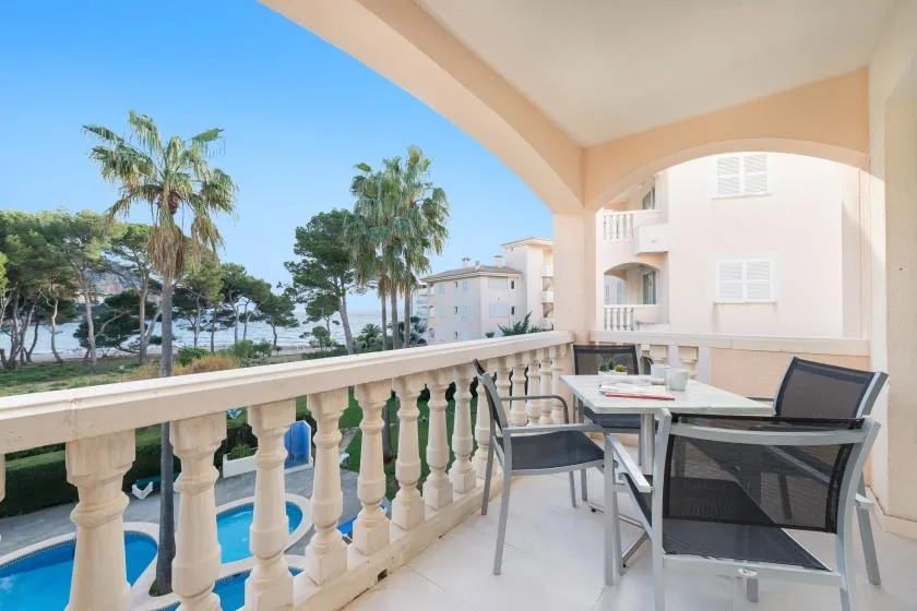 A covered balcony with outdoor seating overlooks a swimming pool and palm trees.