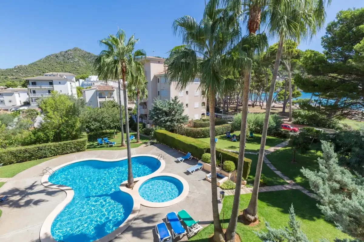 An outdoor swimming pool sits among palm trees and landscaped greenery.
