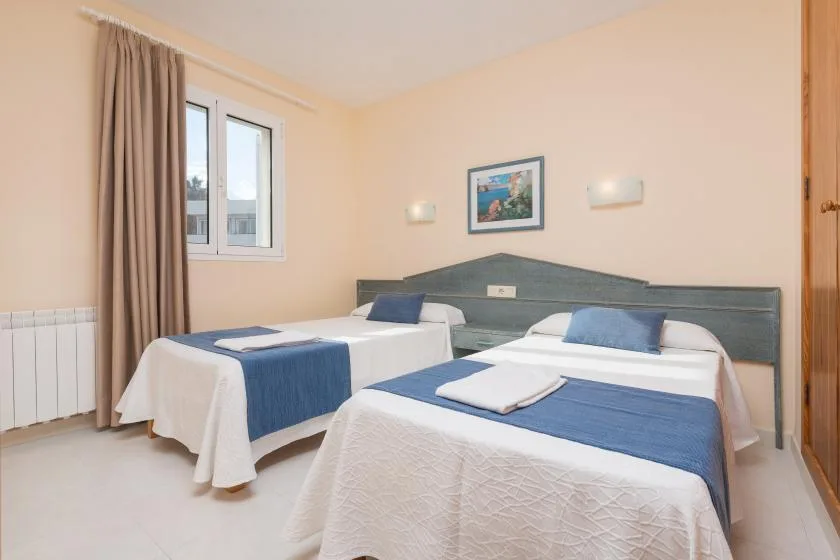 A bedroom with two beds, blue bedspreads, and a window with curtains.