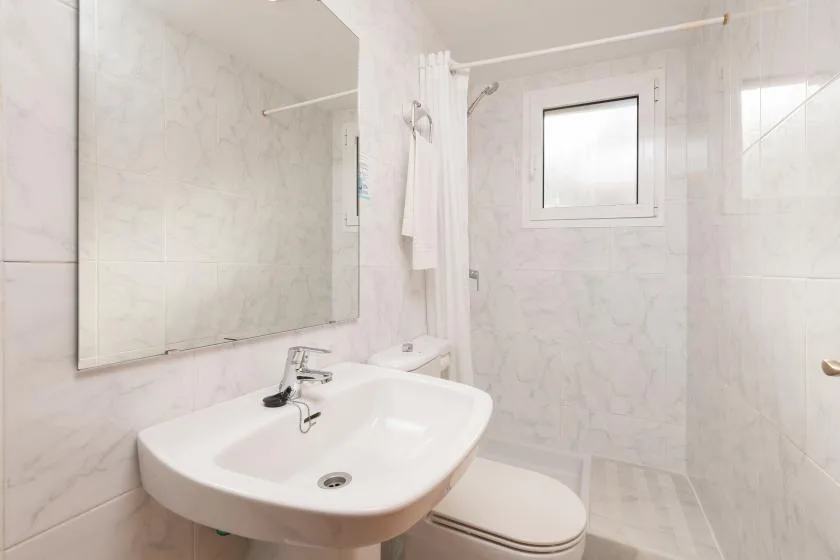 A bright tiled bathroom with a sink, toilet, and small window.