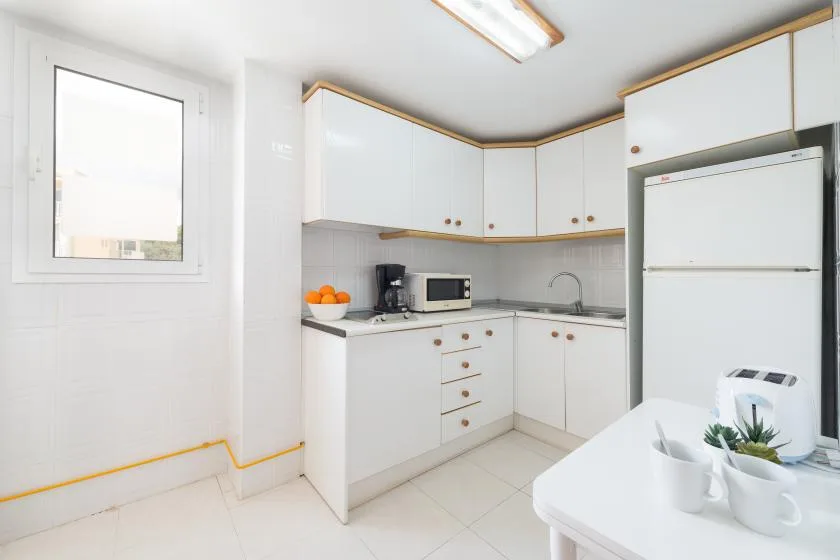 A bright kitchen with white cabinets, a refrigerator, and a small counter table.