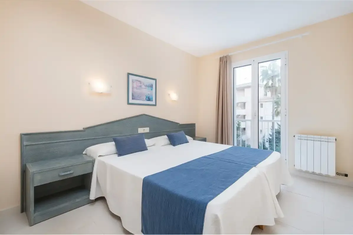 A bedroom with a double bed, blue bedding, and a window.