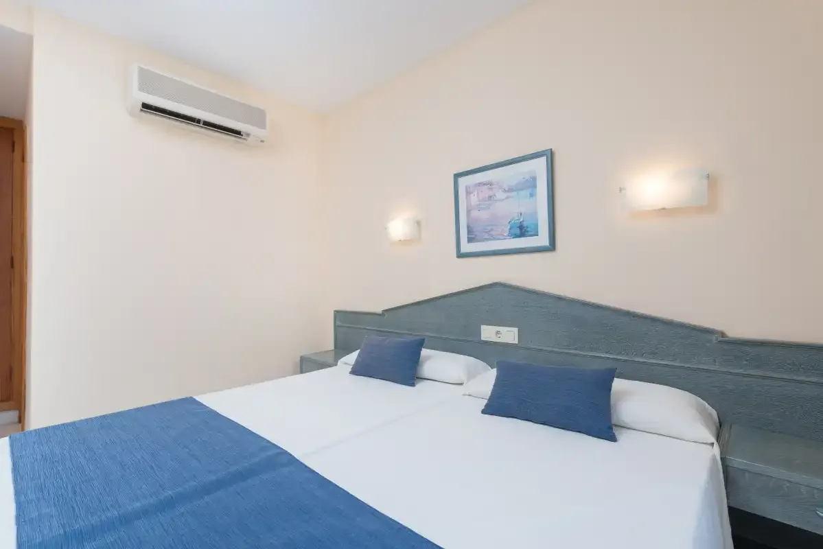 A bedroom with a bed, blue bedding, and a wall-mounted air conditioner.