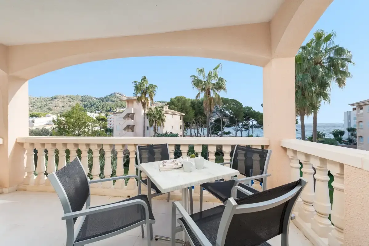 A covered terrace with outdoor seating and views of palm trees and the sea.