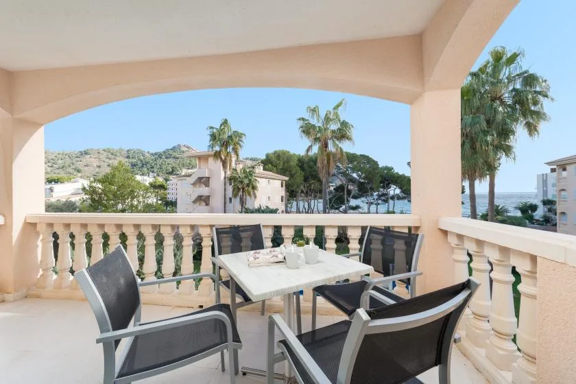 A covered outdoor terrace with seating and a table overlooks palm trees and the sea.