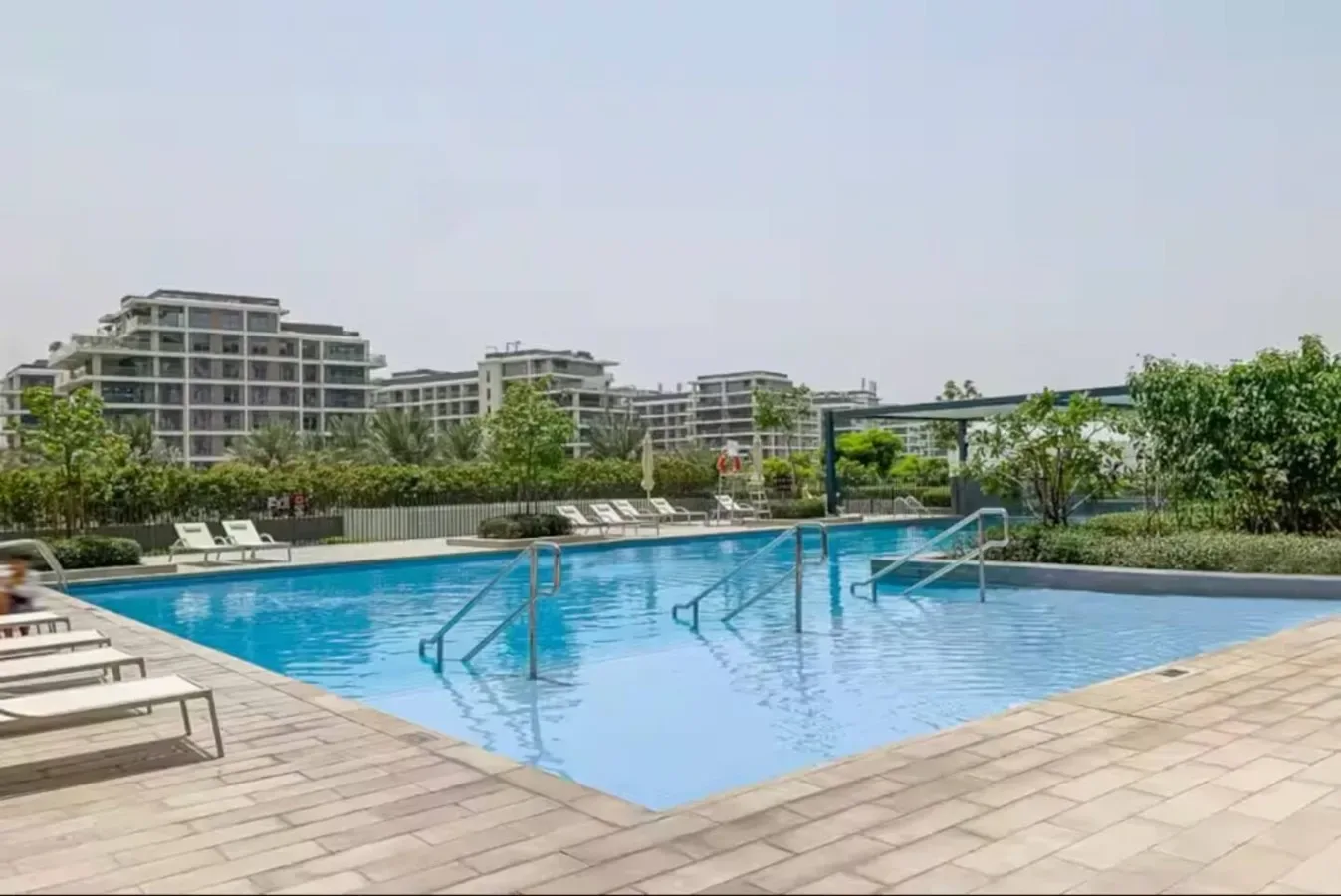 An outdoor swimming pool is surrounded by paved decking and lounge seating.
