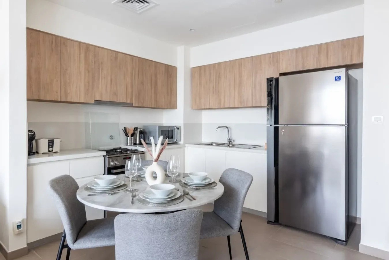 A kitchen and dining area with a set table, wood cabinets, and a refrigerator.
