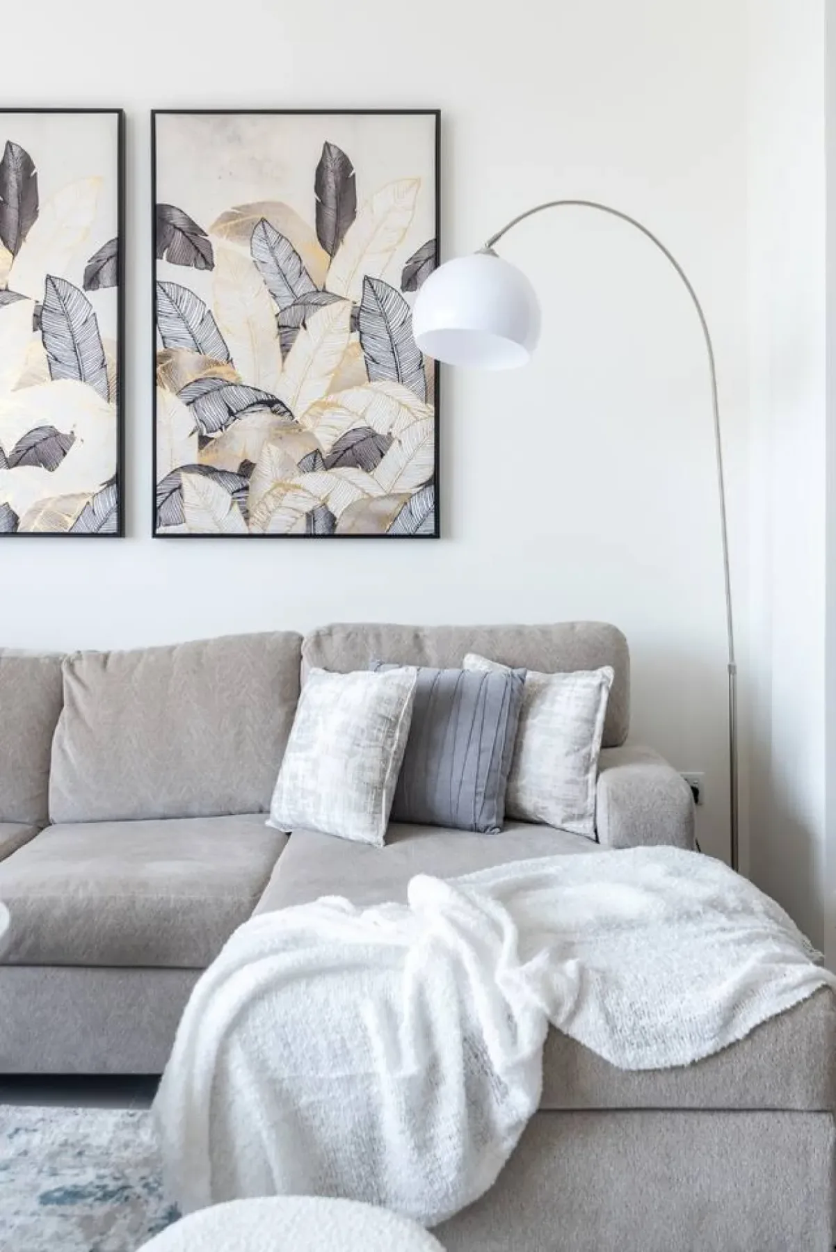A light-colored living room seating area with framed botanical artwork and a draped blanket.